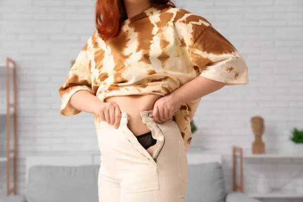 Image of woman trying to do her trousers up after pregnancy weight gain Smallwood